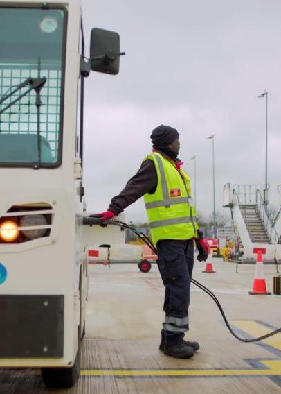 Man in hi viz yellow waistcoat refueling a luggage tug at an airport.